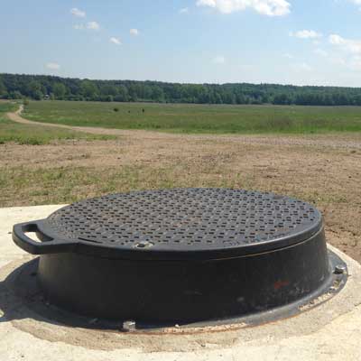 Bolted REVOLUTION manhole cover assembly on a raised concrete structure in a field